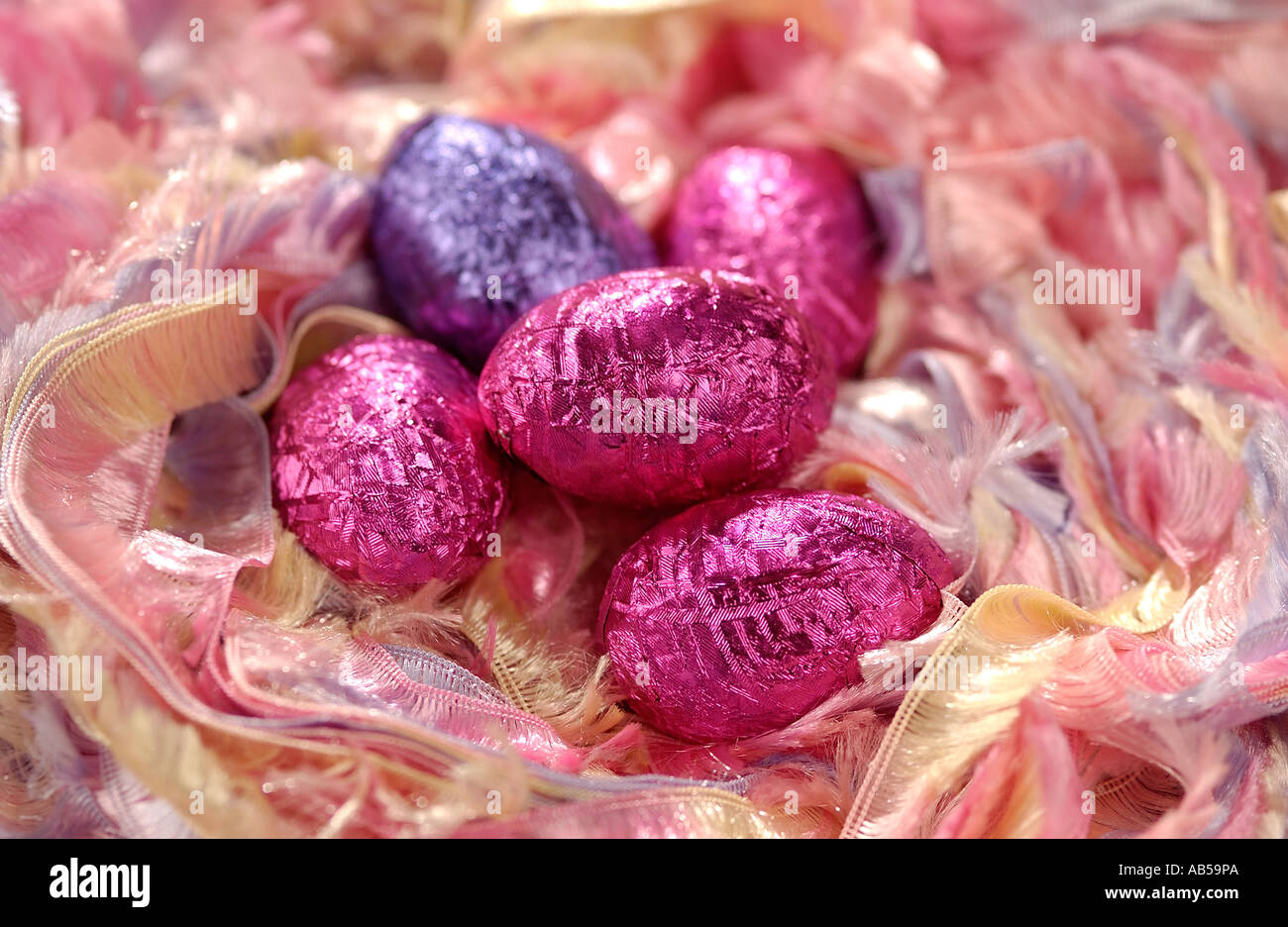 Small chocolate Easter eggs covered in colourful foil laying in a ribbon nest Stock Photo