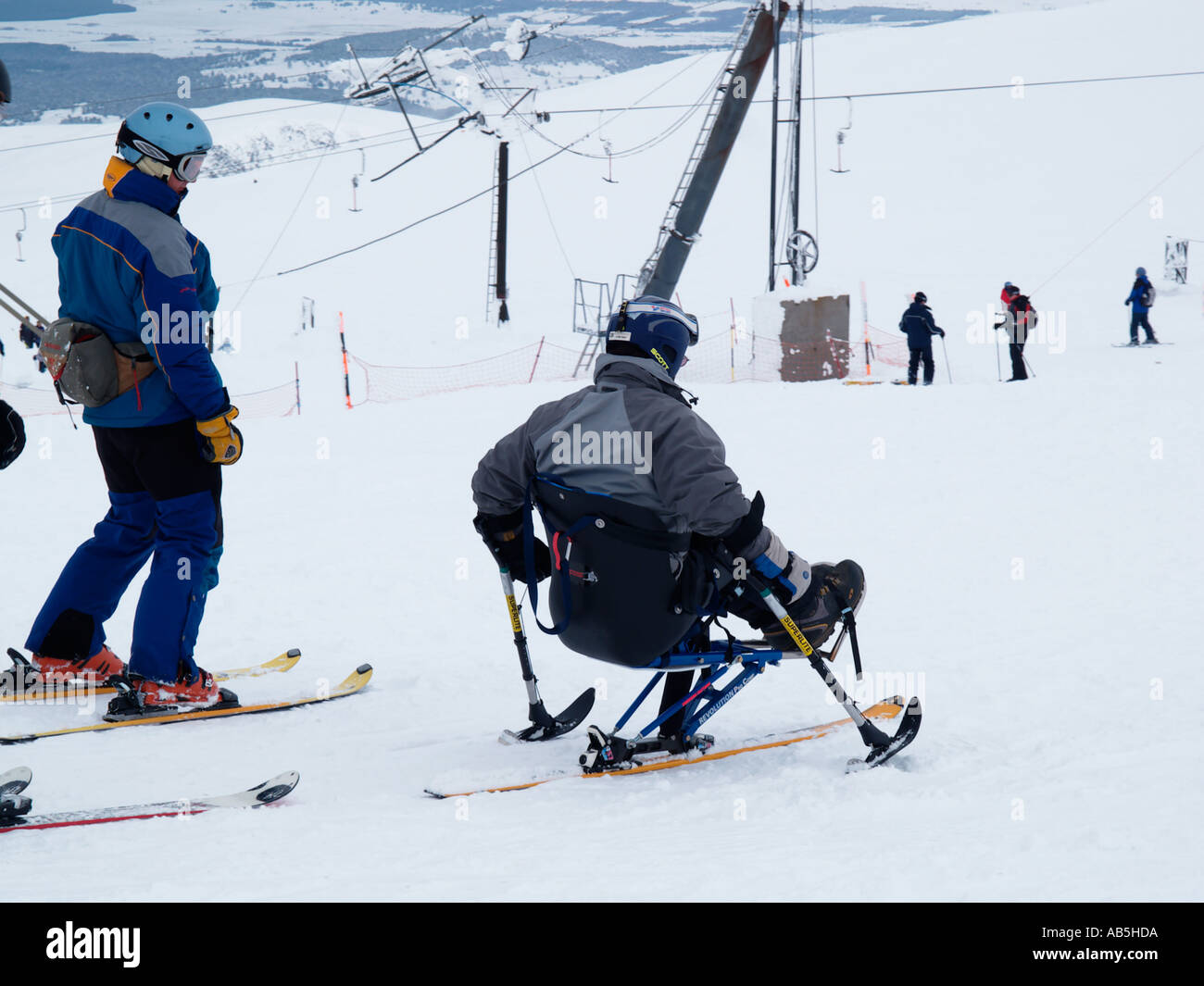 DISABLED SKIER sat on a MONO SKI on Cairngorm mountain ski centre with able bodied skiers Cairn Gorm Highland Scotland UK Stock Photo