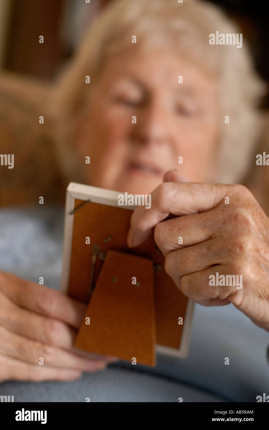 Elderly lady seated looking at old photograph reminiscing looking lonely Stock Photo