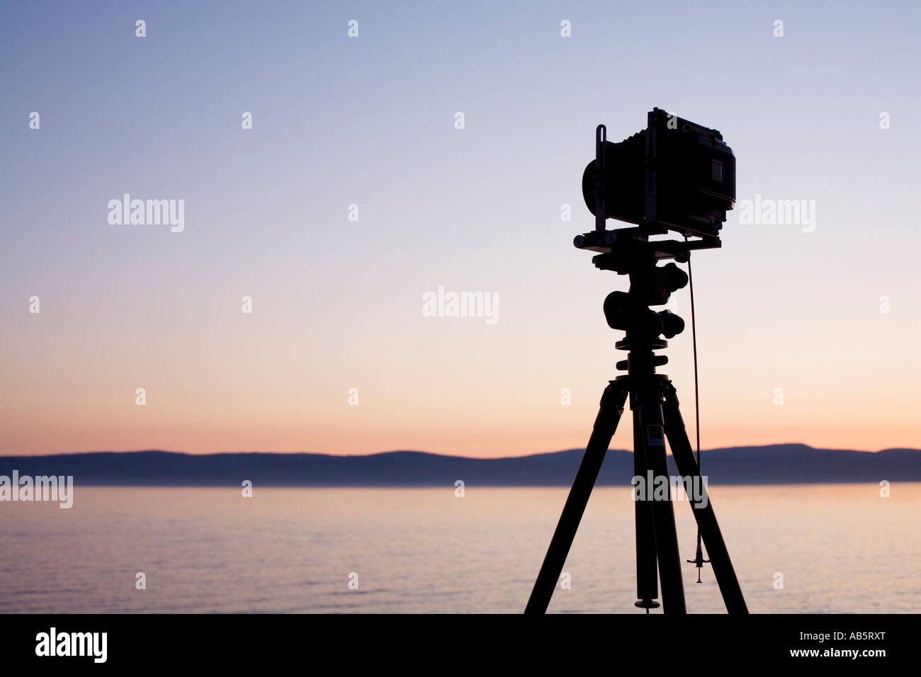 A silhouetted large format camera mounted on a tripod pointing across