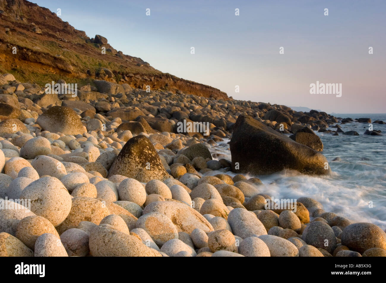 Late evening light on a boulder beach near Nanjulian Cove Cornwall UK Stock Photo