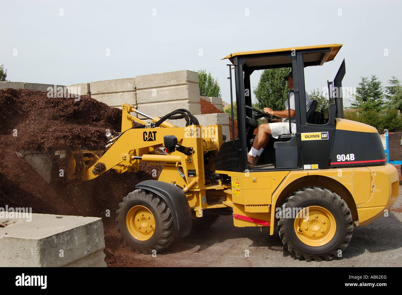 Nursery garden center employee operates a Caterpillar front end loader at a bulk compost plant Stock Photo