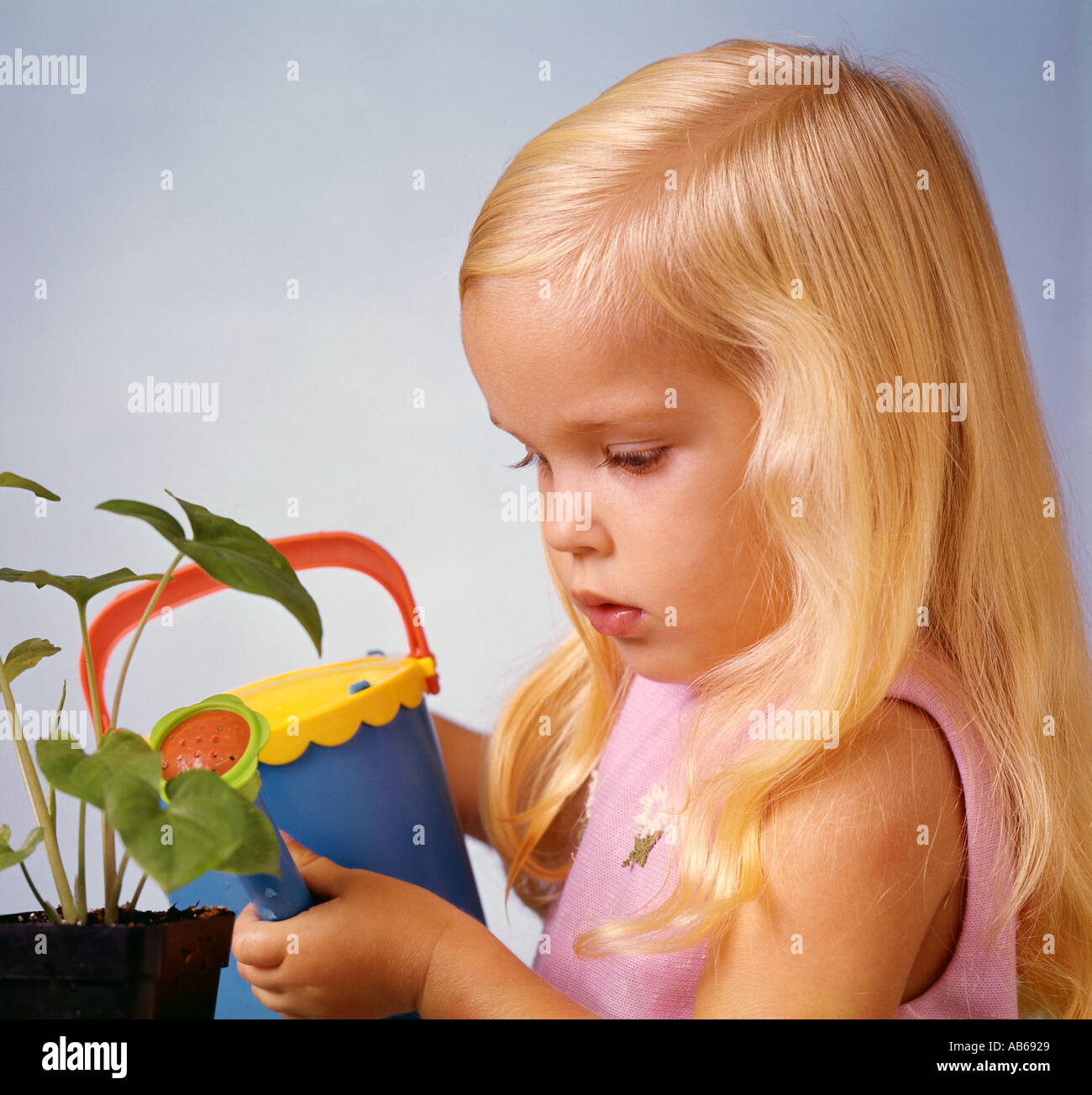 small girl watering tiny plant with toy sprinkling can Stock Photo