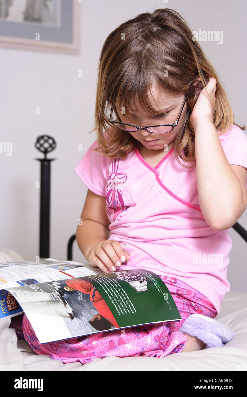 young girl age 4-10 try or pretend to read a magazine with mom's glasses and bored Stock Photo