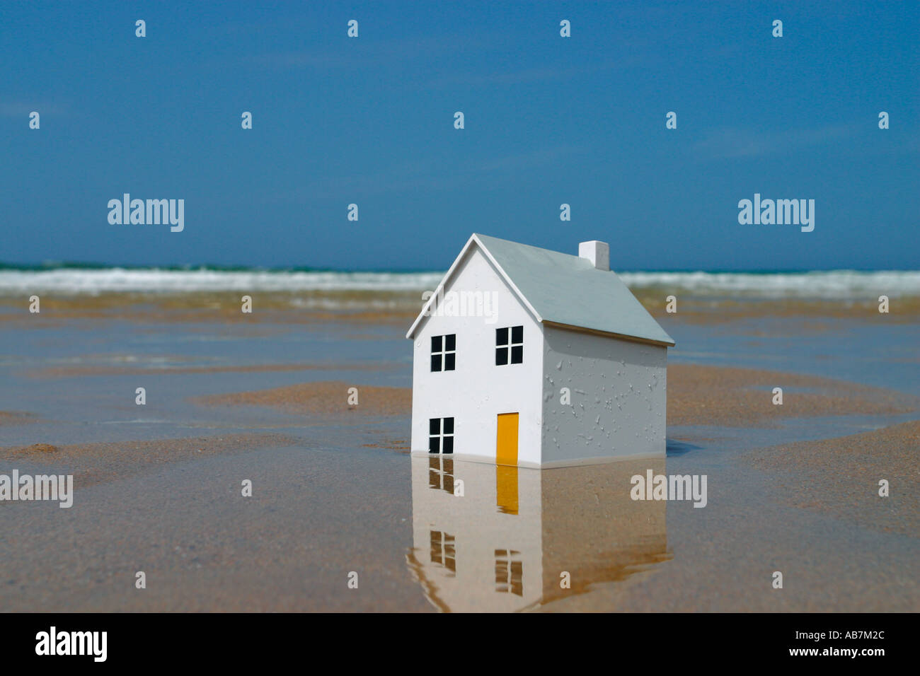 Model house sinking into the sand with ocean waves in the background Stock Photo