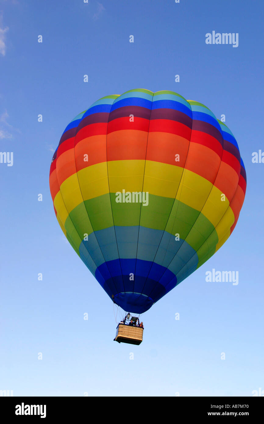 Hot air balloon with rainbow coloured design flying against a blue sky ...