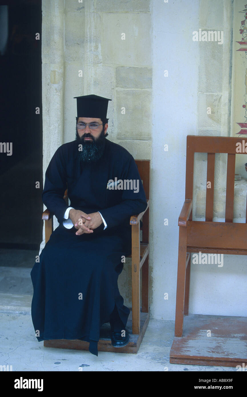 Cypriot clergyman, middle-aged, sitting in long black robe on wooden chair, Cyprus. Stock Photo