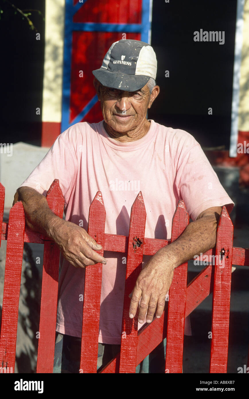 old Mauritian behind red-painted garden gate, wearing a baseball cap, Mauritius, Rodrigues. Stock Photo