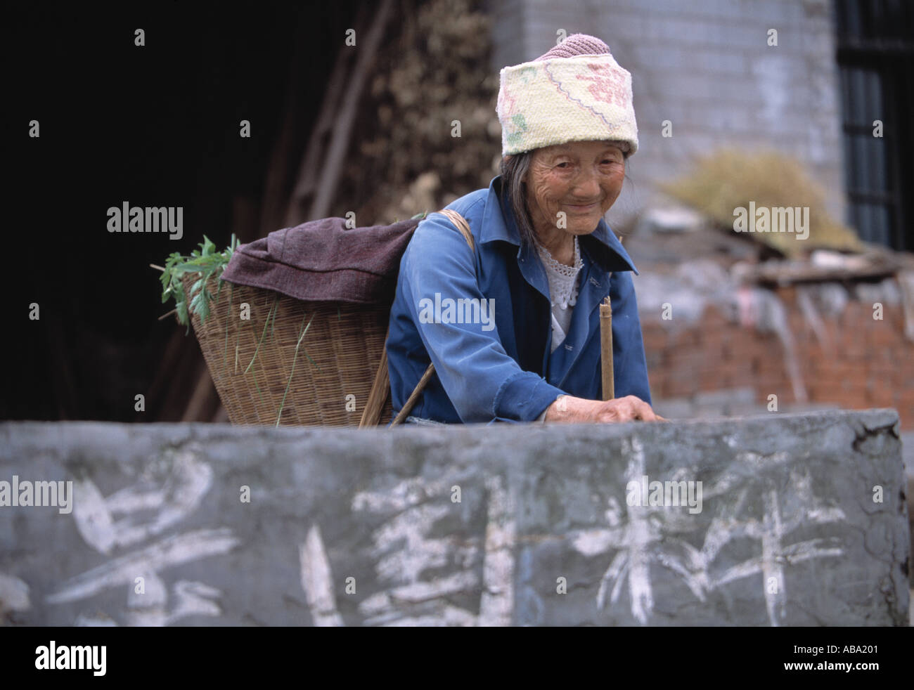 A Ba farmer carrying a basket stands behind a wall in rural China near Wanxian 042103 Stock Photo