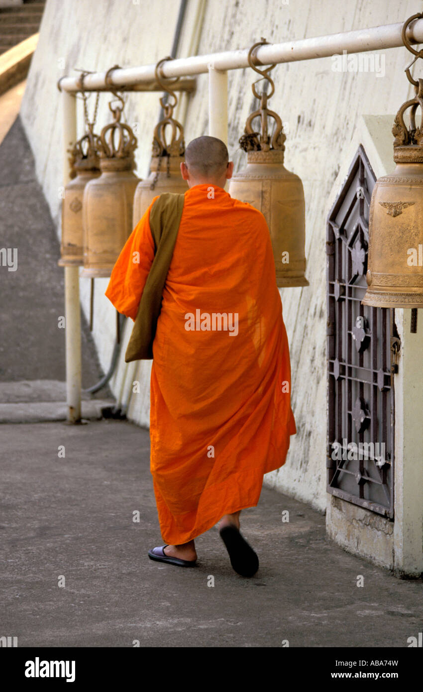 Buddhist monk walking past temple bells hanging from horizontal pole at Wat Saket, aka The Golden Mount, Bangkok, Thailand Stock Photo