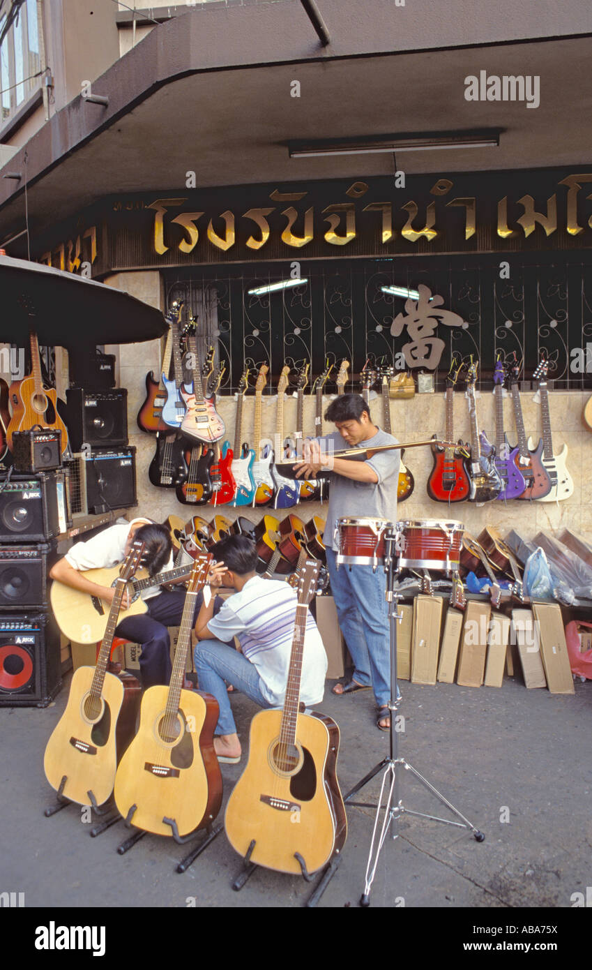 Guitars on sale and men handling playing outside shop in Khlong Road, Bangkok, Thailand Stock Photo