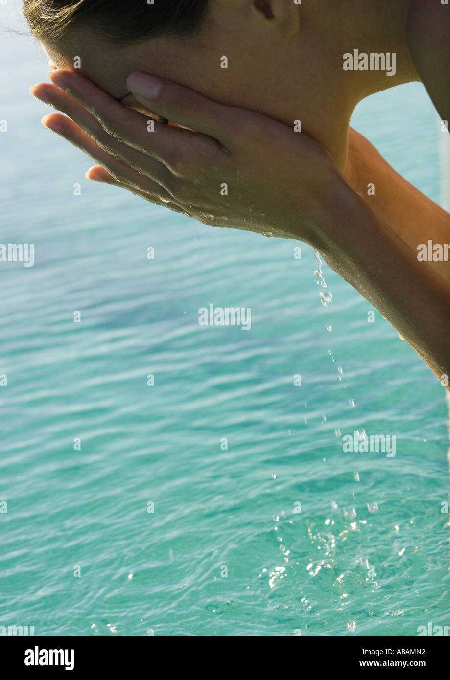 Woman leaning over water, cupping water to face Stock Photo