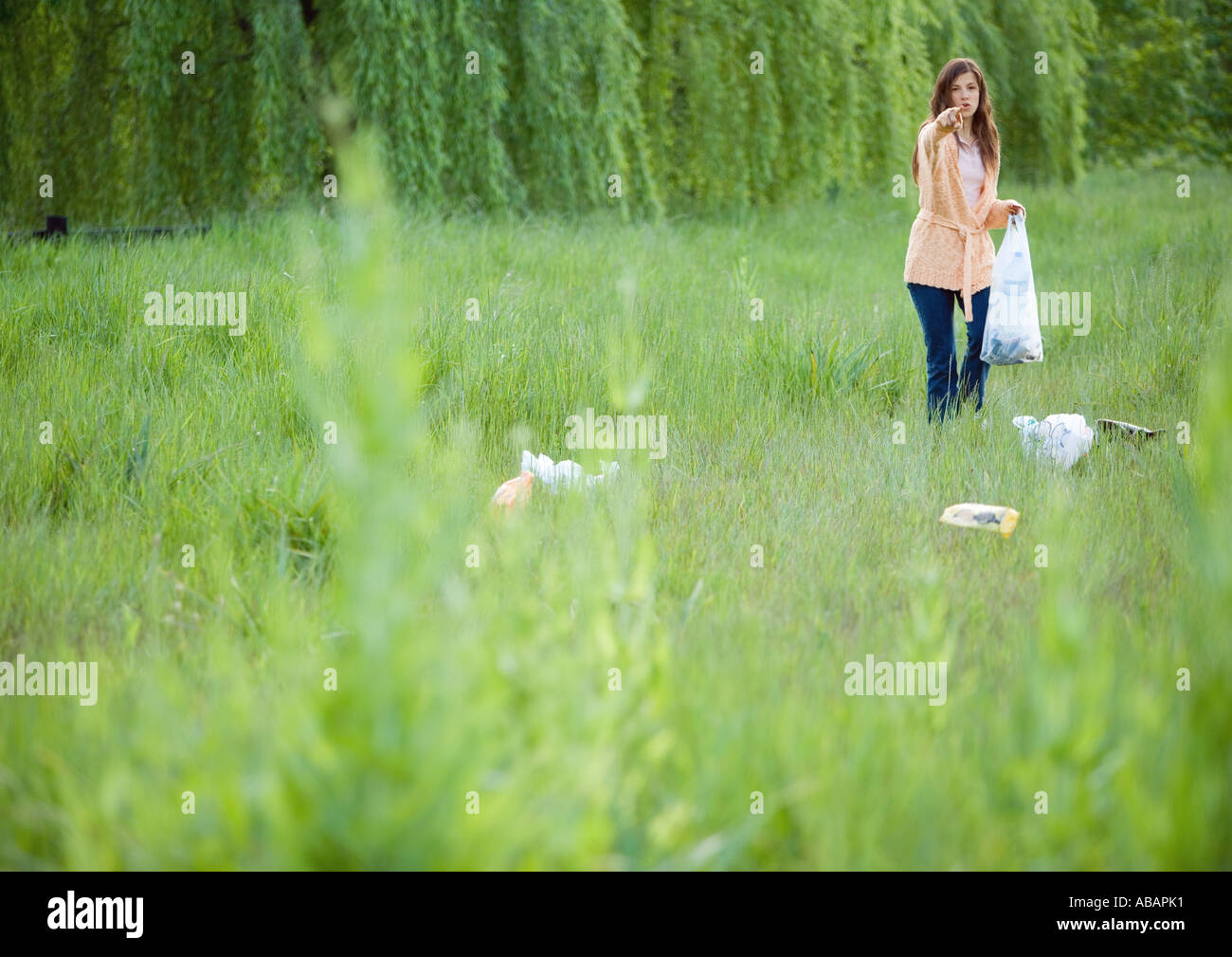 Woman picking up litter in field, pointing at camera Stock Photo Alamy