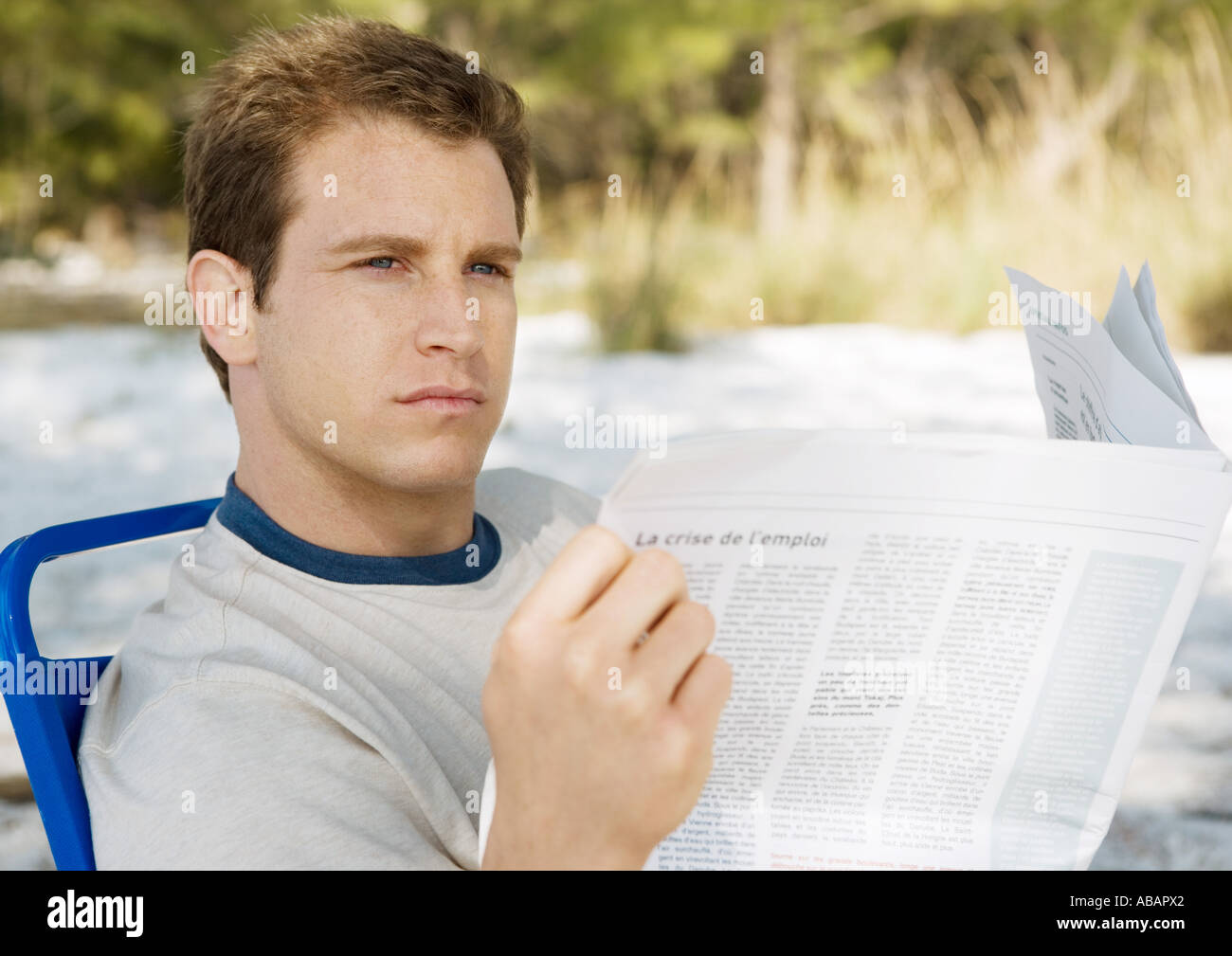 Man looking up from newspaper on beach Stock Photo