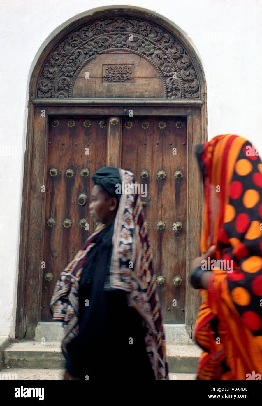 Zanzibar Stone Town Zanzibari women in traditional khangas passing an old wooden carved door Stock Photo