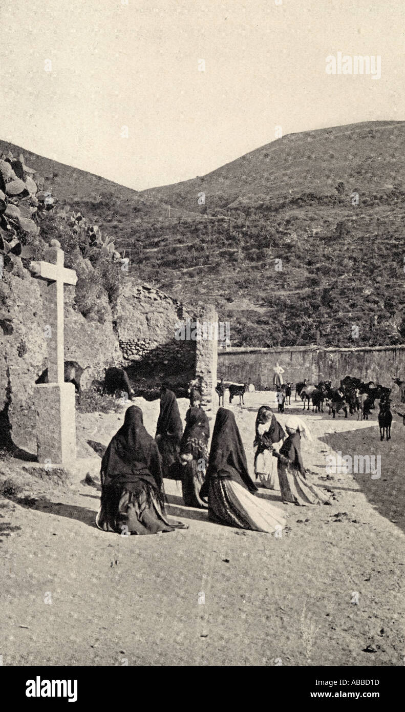Women kneeling in front of cross in a roadside scene in Spain circa 1900 Stock Photo