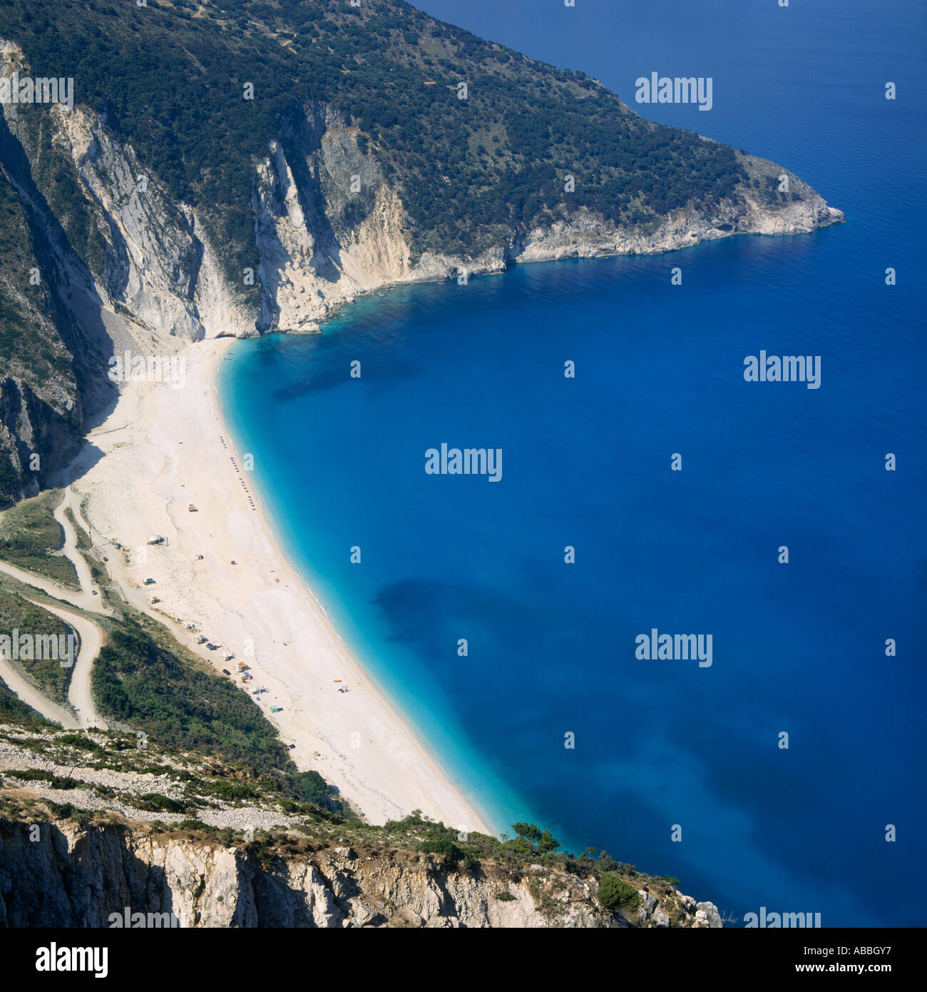 Looking down on bay with clear blue water white sand beach and zig-zag road down hillside Mirtos Cephalonia Island Greek Islands Stock Photo