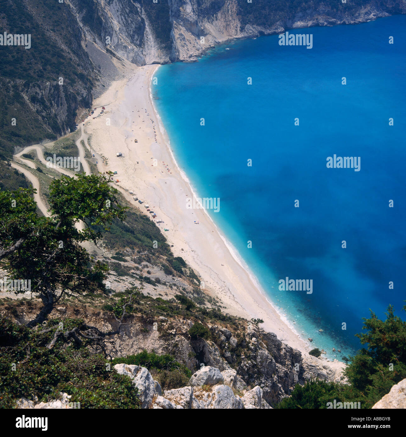 Looking down on bay with clear blue water white sand beach and zig-zag road down hillside Mirtos Cephalonia Island Greek Islands Stock Photo