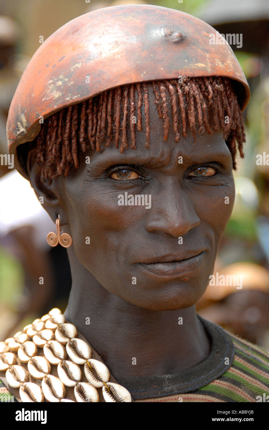 Portrait austere looking woman wearing a chain of kauri mussels and a kalabasse on her head on the market of Keyafer Ethiopia Stock Photo