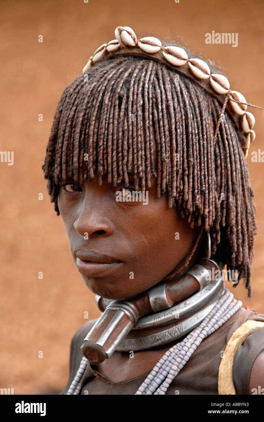 Portrait woman of the Hamar people looks sad and wears a typical clay hairdo and metal and kauri mussel chains at the market of Stock Photo