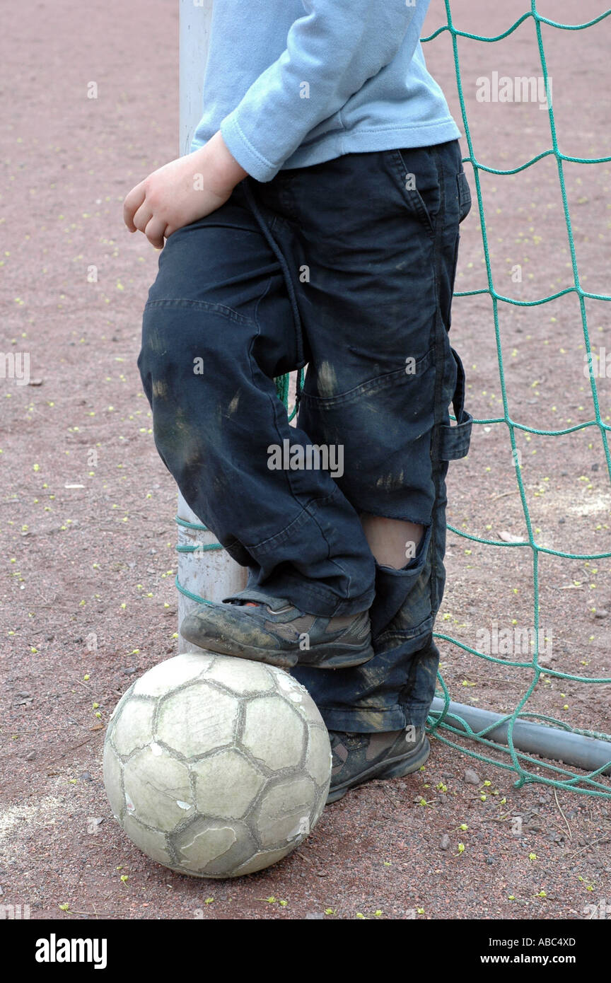 A Boy leaning againt the goal his foot is standing on a ball Stock Photo
