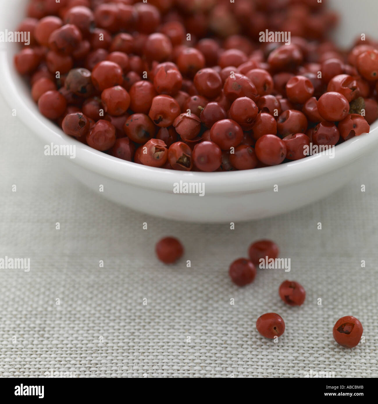 Pink peppercorns in white bowl on linen background Stock Photo