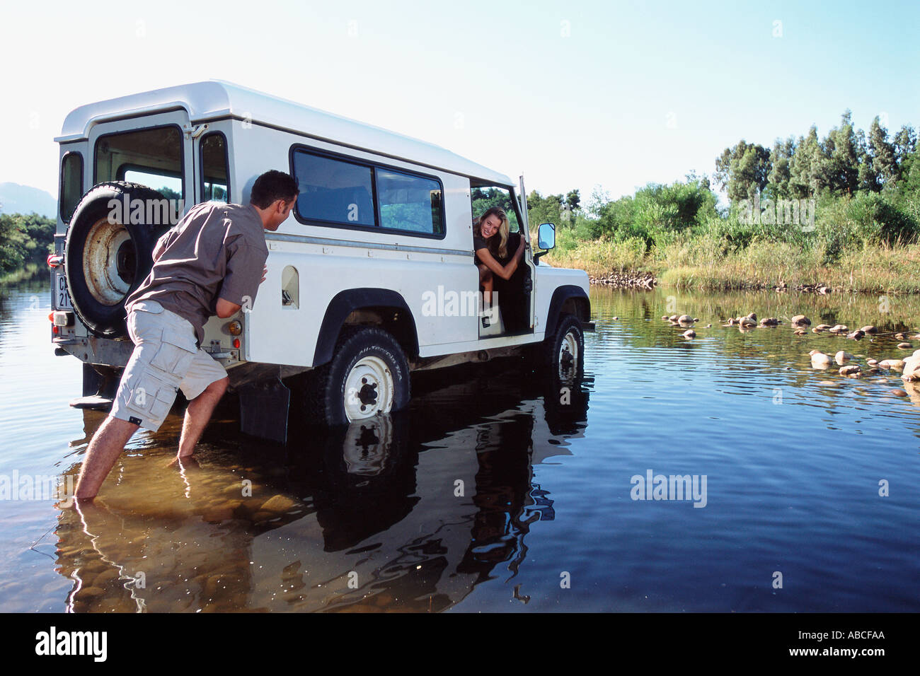 Man pushing a 4x4 across a shallow river Stock Photo