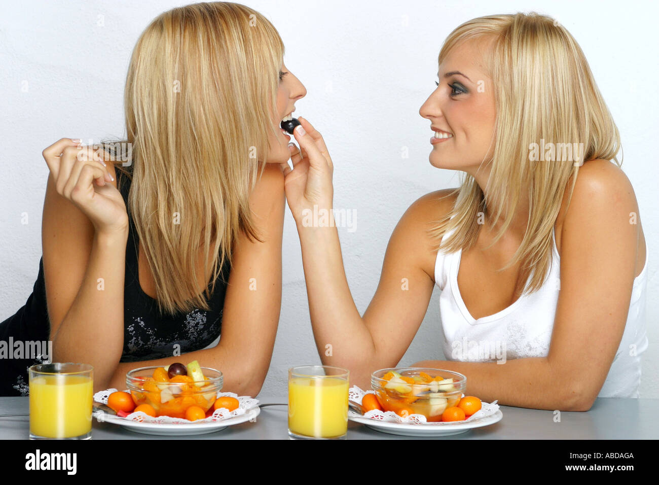 Blond twins feed themselves with fruit salad Stock Photo