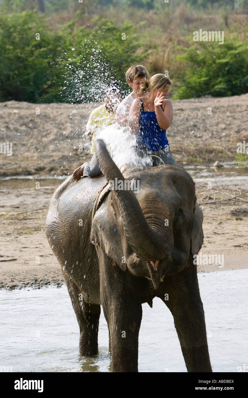 Elephants splash and spray surprising young tourists in river on trek near Pai north Thailand Stock Photo