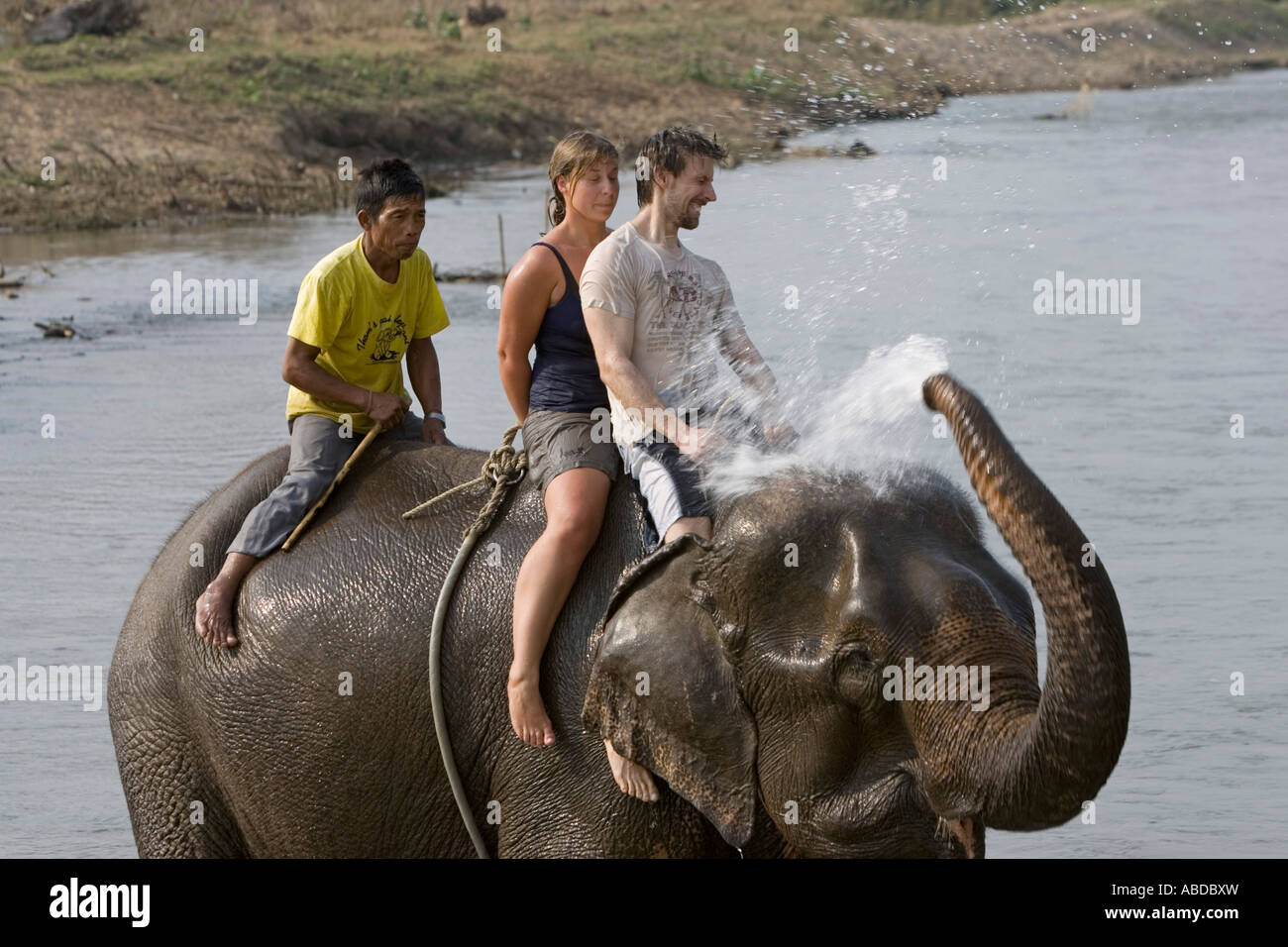 Elephants splash and spray surprising young tourists in river on trek near Pai north Thailand Stock Photo