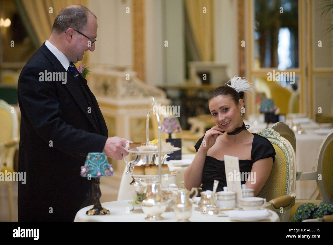 A waiter serves tea to a glamorously dressed woman in the Palm Court at the Ritz Hotel London Stock Photo