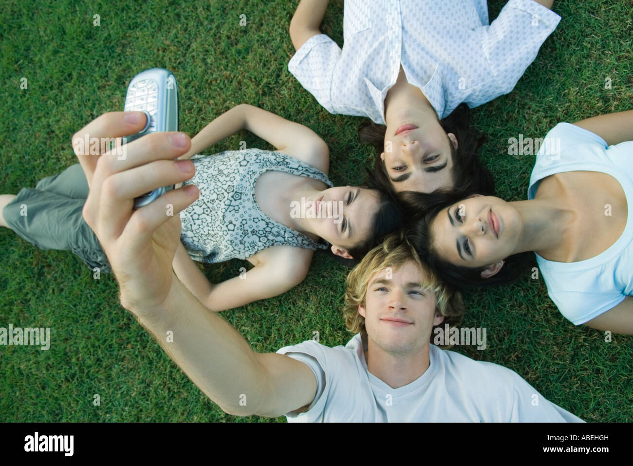 Group of young friends lying on grass, heads together, one young man taking photo with cell phone Stock Photo