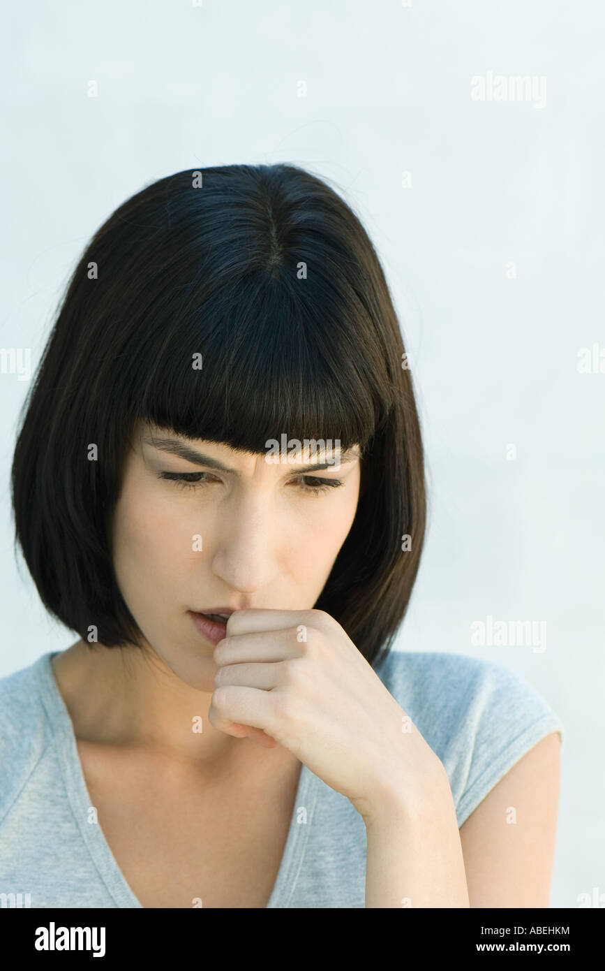 Woman biting thumb and looking down, head and shoulders, portrait Stock Photo