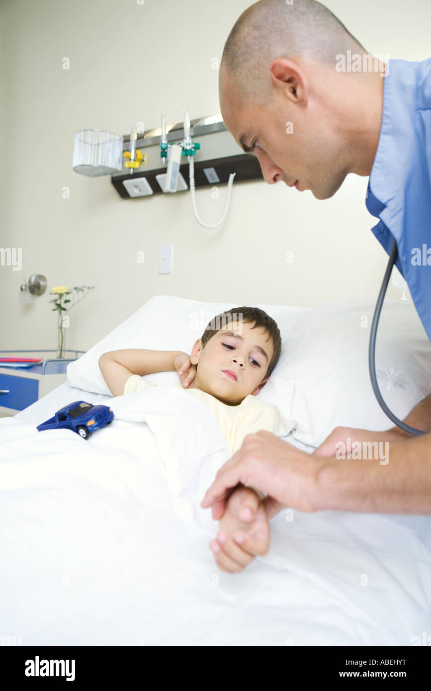 Boy lying in hospital bed, intern holding boy's arm Stock Photo Alamy