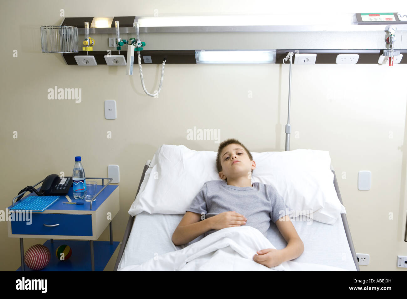 Boy lying in hospital bed, holding stomach Stock Photo