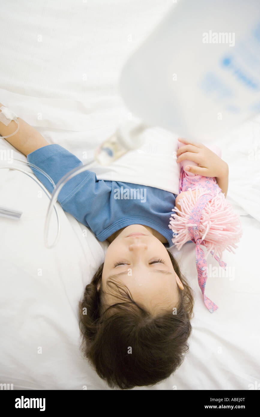 Girl lying in hospital bed holding doll Stock Photo
