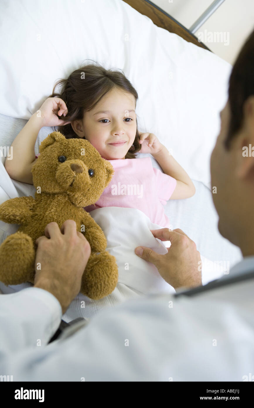 Girl lying in hospital bed, smiling up at doctor Stock Photo