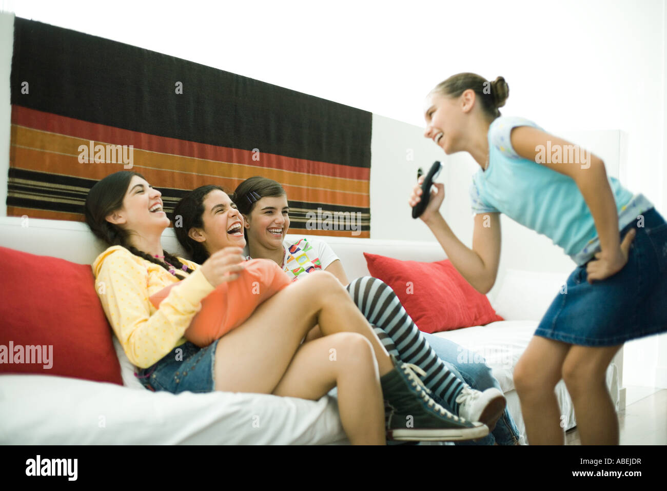 Preteen girl singing into remote control, friends laughing Stock Photo