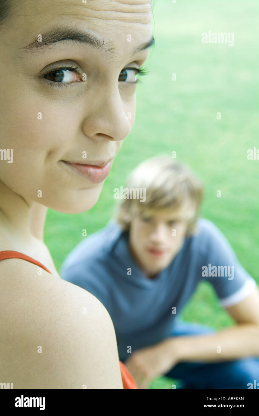 Teen girl looking over shoulder at camera, raising eyebrows, male friend in background Stock Photo