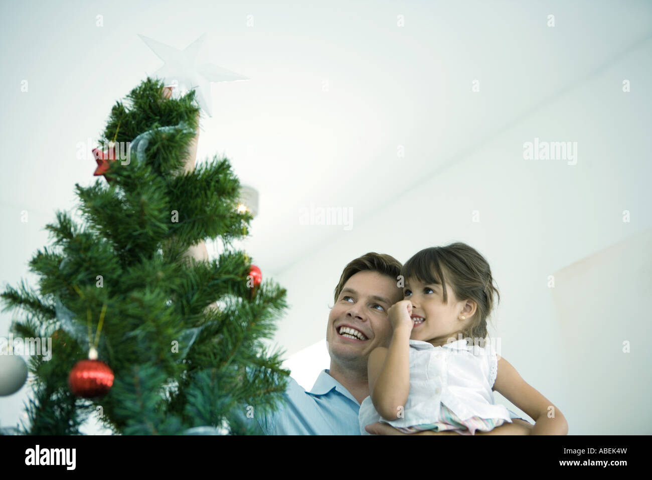 Father and daughter placing star on top of Christmas tree Stock Photo