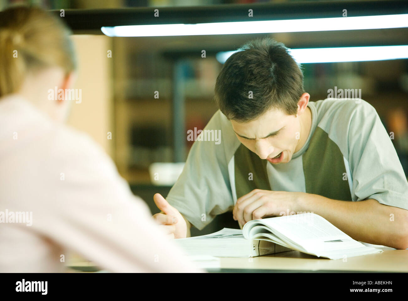Male college student sitting in library, studying and yawning Stock Photo