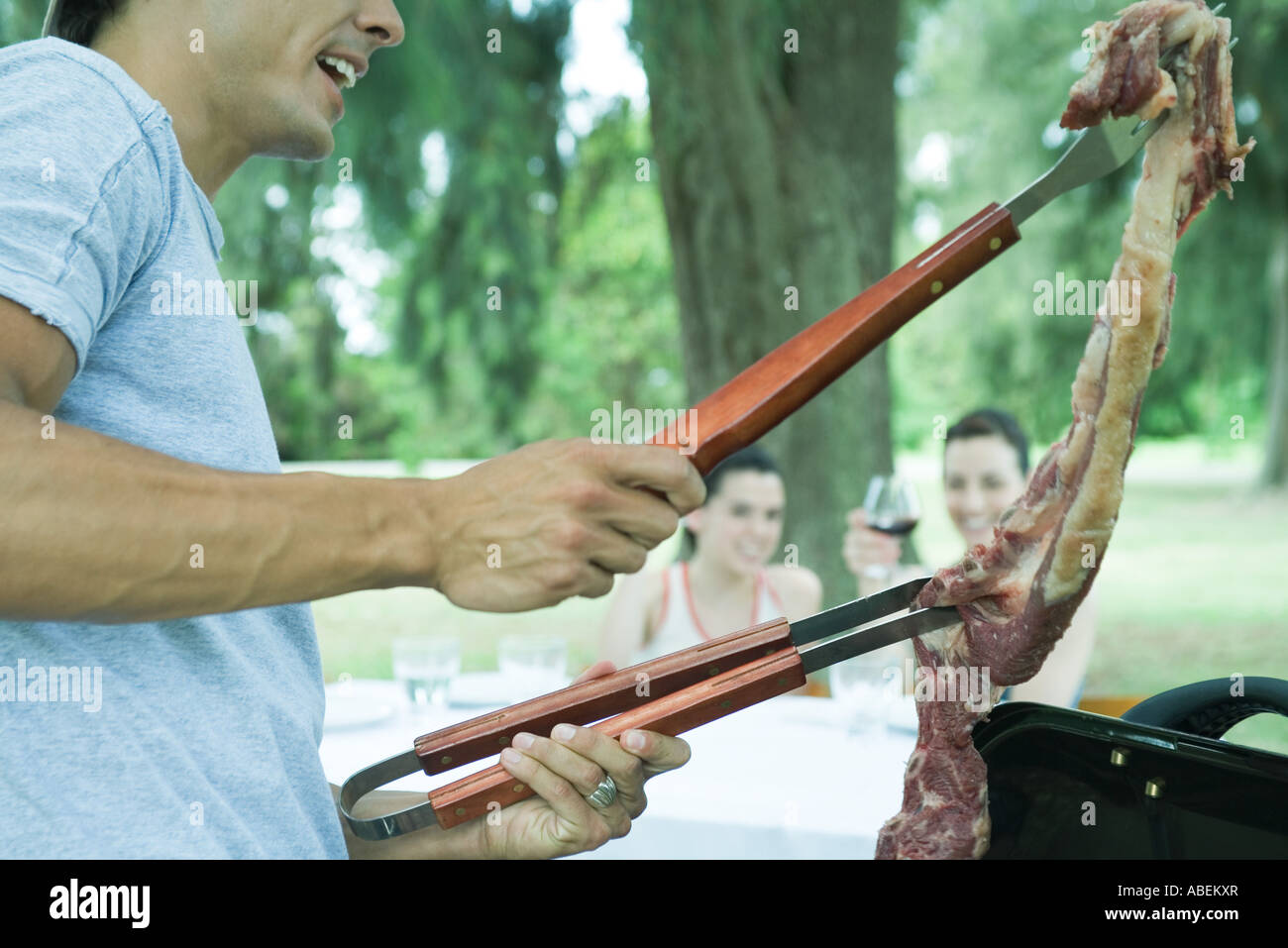 Man holding up piece of meat over barbecue Stock Photo
