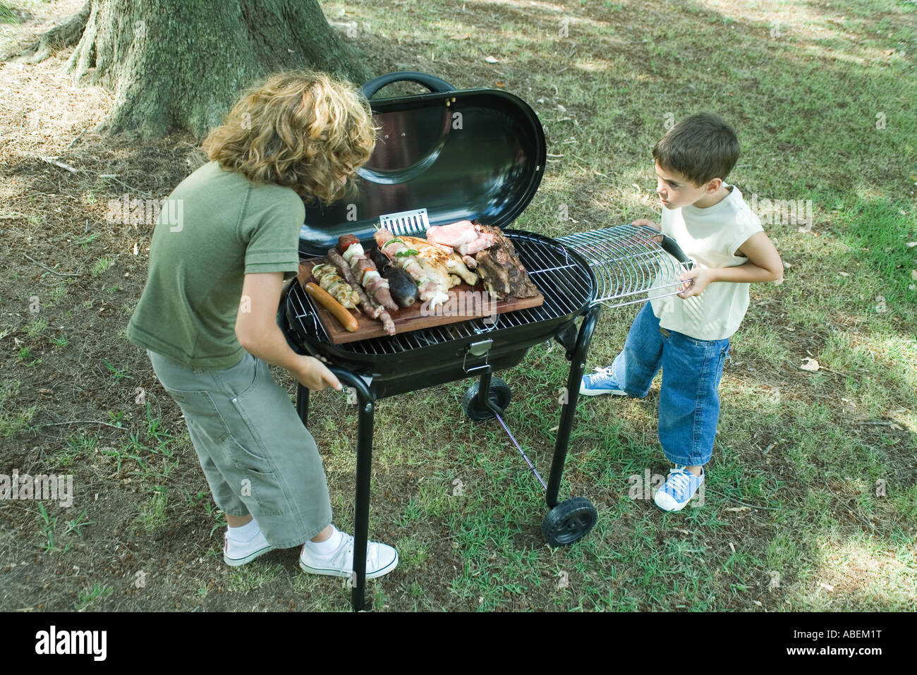 Two boys standing next to tray of grilled meat on barbecue Stock Photo