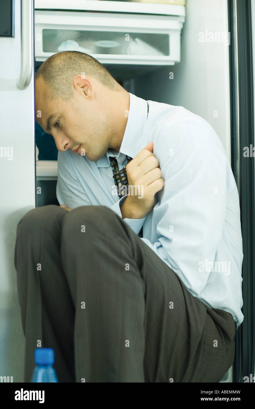 Man sitting in front of open refrigerator in fetal position Stock Photo