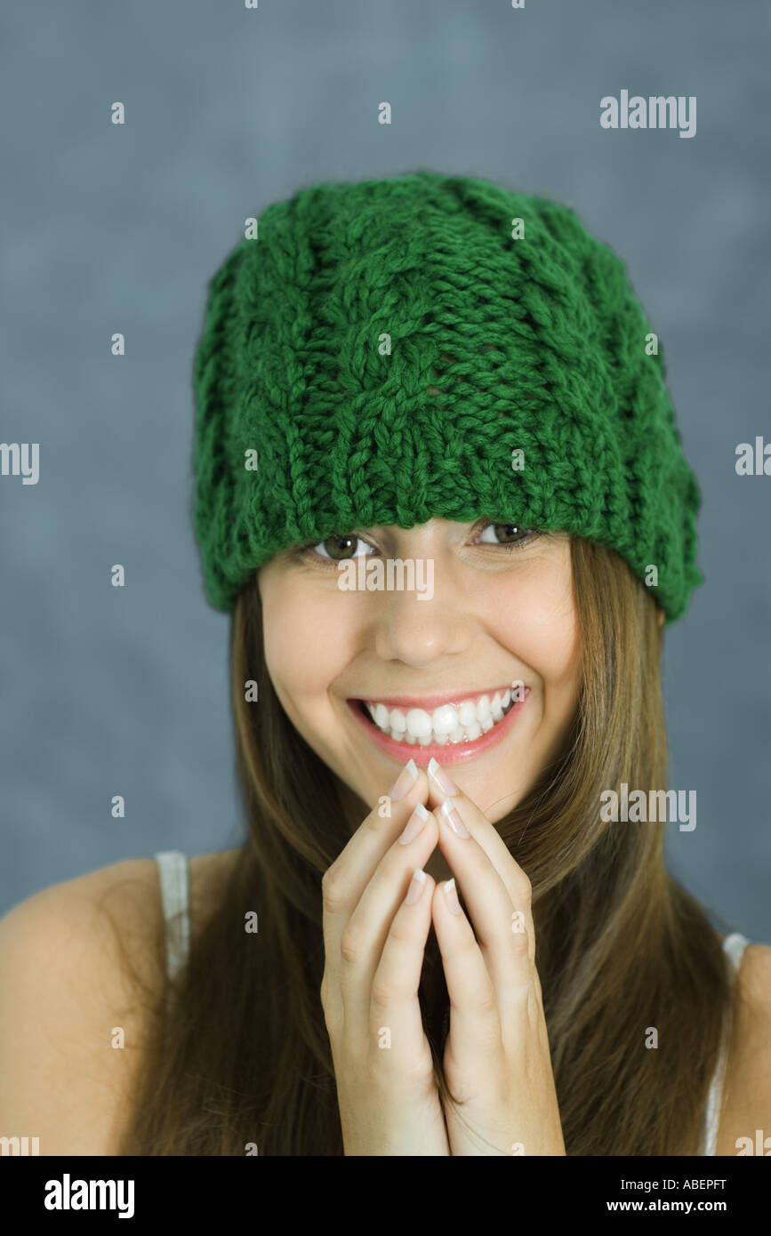 Teen girl wearing knit hat, hands clasped in front of chin, smiling at