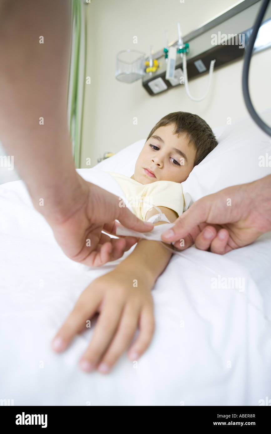 Boy lying in hospital bed, having IV taped to arm Stock Photo