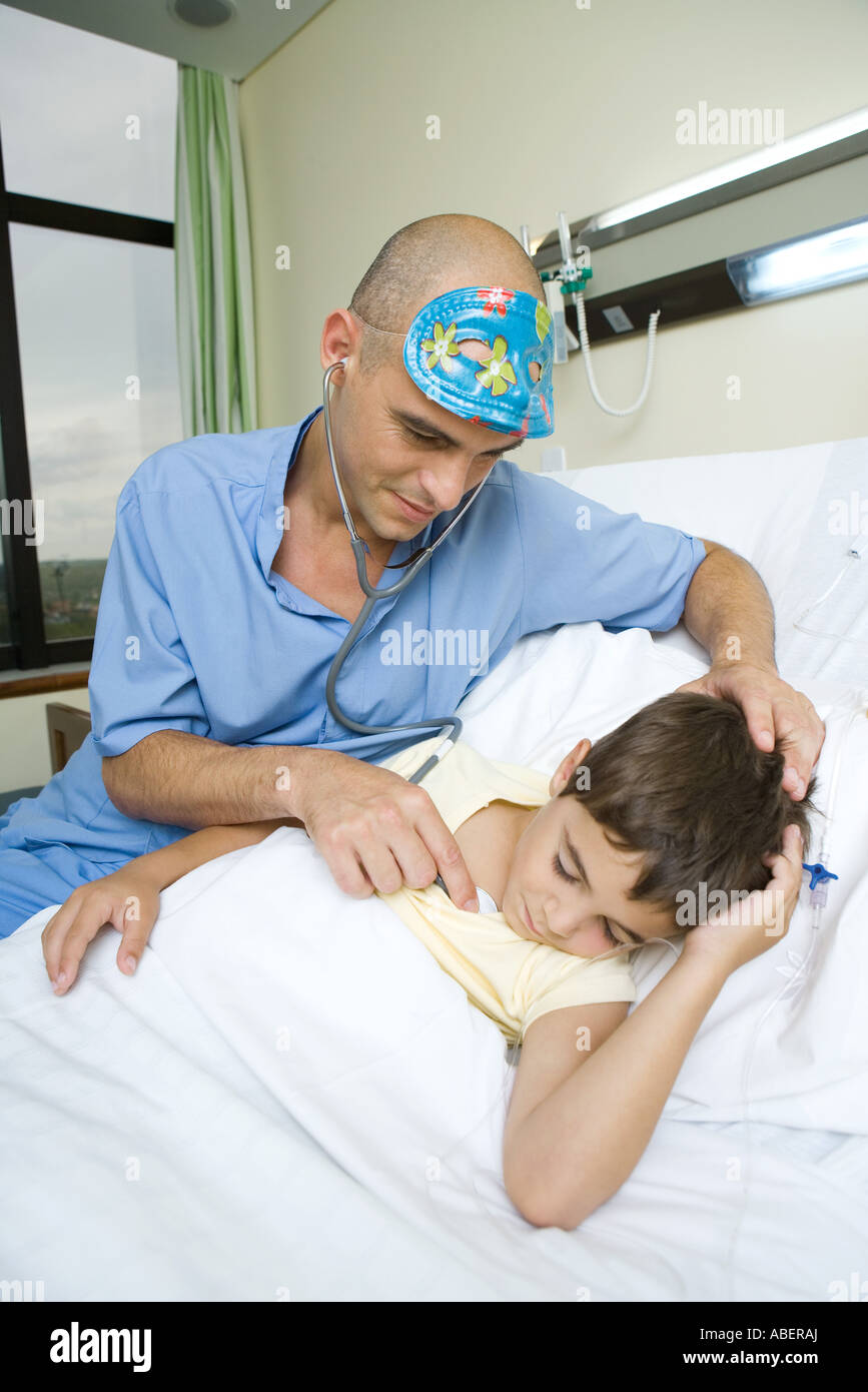 Boy lying in hospital bed, sleeping, doctor holding stethoscope to boy
