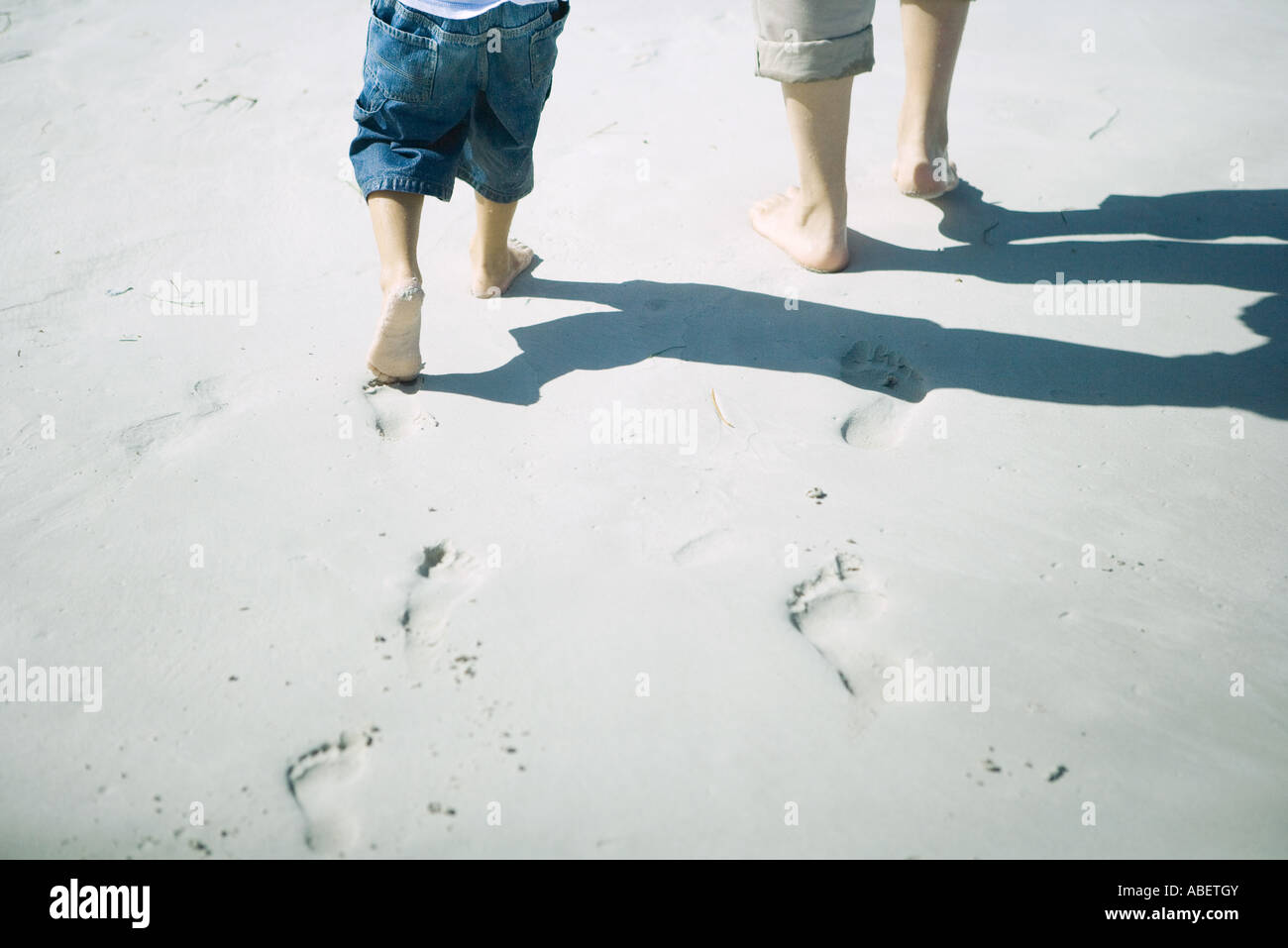Child and adult walking on sand, low section Stock Photo