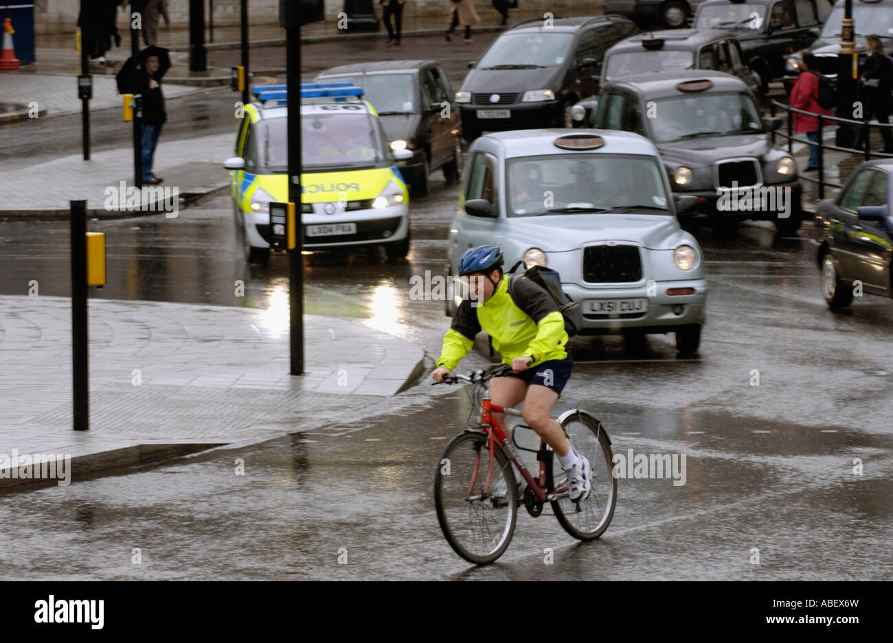 Commuter cyclist with black cab London taxis in rain Trafalgar Square, London, UK Stock Photo
