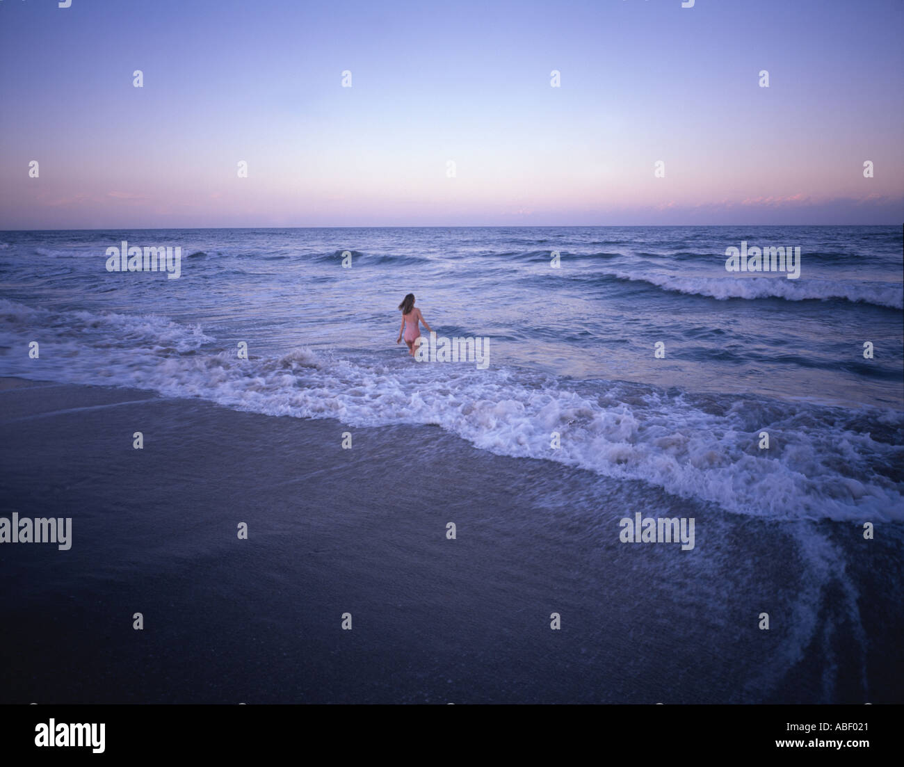 Woman in surf at sunset Stock Photo